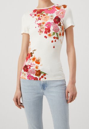 Short-sleeve white t-shirt with colorful floral print in pinks, reds, and oranges. Fitted design, soft texture. Paired with light blue jeans.