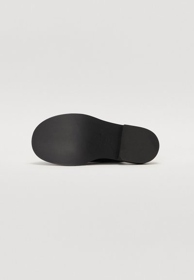 Black shoe sole featuring a smooth, matte finish with rounded edges. Notable logo detail embossed on the heel area.
