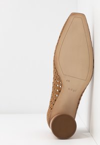 Chaussure à talon tressée beige avec un dessous rond et texturé. Semelle beige lisse avec le nom de la marque "hög" et la taille "4½" imprimés à l'intérieur.