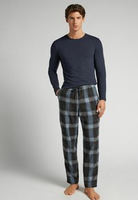 Långärmad topp i marinblått kombinerad med grå och blå rutiga flanellpyjamasbyxor med elastisk midja och dragsko. Barfota.