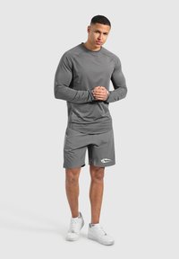 Grau sportliches Langarmshirt und Shorts, aus feuchtigkeitsableitendem Material. Mit einem Logo auf den Shorts und einer figurbetonten Passform.