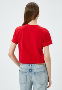 Röd kort t-shirt i mjuk bomull, med korta ärmar och rund halsringning. B�ärs med ljusblå högmidjade jeans.