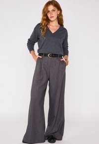 Pull gris à col en V avec des manches longues associé à un pantalon large à carreaux gris taille haute. Ceinture noire avec boucle circulaire et chaussures noires.