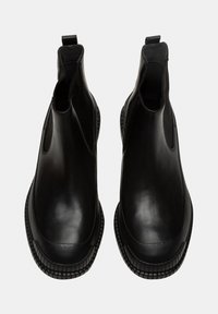 Stivali alla caviglia in pelle nera con pannelli elastici laterali e linguette. Presentano una suola in gomma testurizzata con punta rotonda e design minimalista.