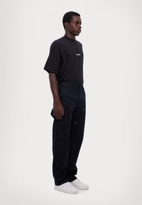 Črna oversized majica s belim logotipom, v kombinaciji z mornarsko modrimi hlačami s srebrnimi detajli, obuta v bele superge. Preprost, vsakdanji outfit.
