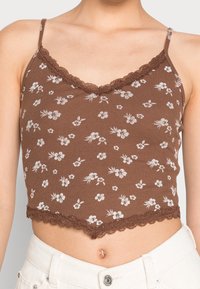 Top corto de estampado floral marrón hecho de tela acanalada, con un borde de encaje con forma de ondas a lo largo del escote y el dobladillo inferior. Tirantes finos.