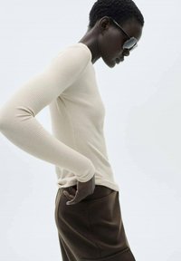 Beige gestreiftes Langarmoberteil, körpernah geschnitten, kombiniert mit braunen hochtaillierten Hosen, die eine glatte Textur und ein minimalistisches Design zeigen.