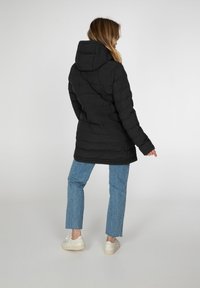 Sort pufferjakke med hætte, med kviltet tekstur og elastiske detaljer i taljen, båret med lyseblå jeans og hvide sneakers.