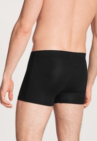 Boxer shorts neri in cotone con un design aderente, superficie liscia e vita piatta. Mostrati da dietro, rivelando le aperture delle gambe.