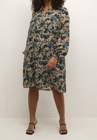 Abito floreale con scollo a V, maniche lunghe e vestibilità ampia. Presenta un motivo multicolore di fiori blu e verdi su uno sfondo beige.