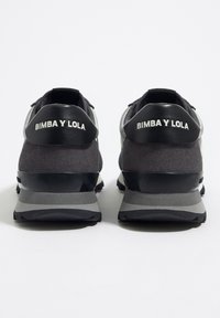 Schwarze und graue Sportschuhe haben ein Obermaterial aus Wildleder, kontrastierende glänzende Akzente und eine Gummisohle mit strukturierten Mustern. Branding auf der Ferse.