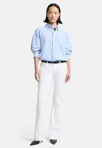 Camicia button-up azzurro chiaro con tasca frontale e maniche arrotolate, abbinata a jeans bianchi a zampa d'elefante e tacchi neri a punta.