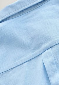 Hellblaues Leinengewebe mit einer weichen, strukturierten Oberfläche. Verfügt über dezente Karomuster und einen umgeschlagenen Kragen. Minimalistisches Design.