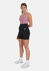 Pink sports bra and black high-waisted shorts made from stretchy material. Features logo accents, and model wears sporty white shoes with socks.