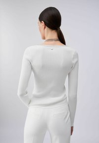 Pull blanc côtelé à manches longues, orné de clous décoratifs le long de l'encolure. Le tissu semble doux avec une silhouette ajustée.