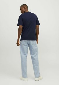 Mørkeblå bomulds t-shirt med korte ærmer, båret med lyseblå løstsiddende jeans og hvide sneakers, set fra bagsiden.