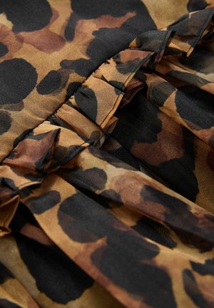 Tissu à motif léopard avec des nuances de marron et de noir, doté d'une texture plissée et de détails volants le long des bords. Matériau doux et fluide.