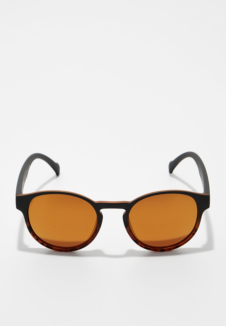 Okrągłe okulary przeciwsłoneczne z brązowymi szkłami, czarną plastikową oprawą oraz akcentami w kolorze żółwia na obrzeżach. Gładka faktura i średniej szerokości zauszniki.