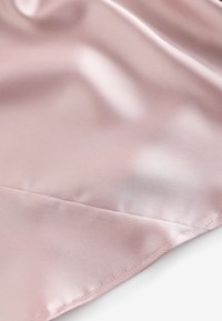 Lyserødt satin stof med glat, skinnende tekstur og subtil syning langs den nederste kant på en hvid baggrund.