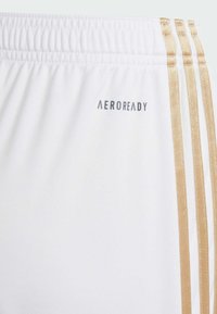 White sports shorts with a textured finish, featuring three gold stripes along the side and a gray "AEROREADY" logo near the waistband.