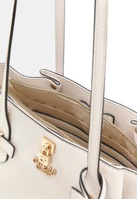 Weiße Ledertasche mit schwarzen Akzenten, zwei Griffen und einem goldfarbenen Logo. Das Innere verfügt über mehrere Fächer mit Reißverschlussverschlüssen.