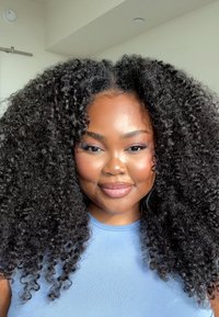 Krøllete svart hår rammer et glatt ansikt, komplementert av en lyseblå tettsittende topp. Huden har en blank finish som fremhever naturlige trekk.