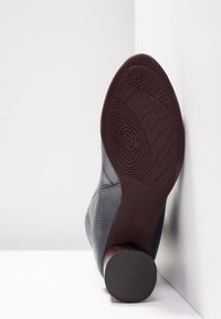 Semelle d'une chaussure à talon texturée de couleur marron foncé avec un motif de bande de roulement circulaire, photographiée sur un fond blanc en coin.