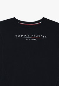 Czarny sweter z okrągłym dekoltem, z białym i czerwonym graficznym logo "TOMMY HILFIGER NEW YORK" na wysokości klatki piersiowej. Gładka struktura.