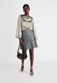 Satin olive green blouse with draped neckline, paired with a gray pleated skirt. Sheer brown handbag and strappy cream platform heels complete the look.