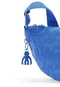 Blå tygväska med en texturerad blommönstring och en plastblå apa-formad charm fäst vid ett nyckelring på remmen.