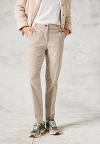 Beige lätta byxor med framfickor, slim fit, i kombination med gröna och beiga sneakers. Har en knäppning och en subtil textur.