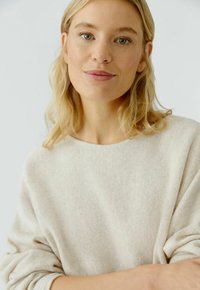Beige Strickpullover mit lockerer Passform, weitem Ausschnitt und gerippter Textur, mit leicht umgeschlagenen Ärmeln und dezenten Farbnuancen im Stoff.