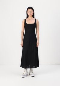 Rochie neagră, fără mâneci, cu decolteu pătrat, cu un corset ajustat și o fustă maxi fluidă. Purtată cu adidași albi cu talpă înaltă și șosete cu model.