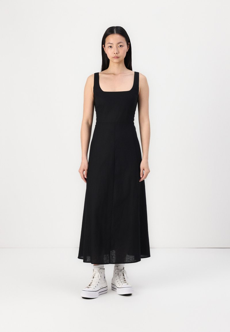 Rochie neagră, fără mâneci, cu decolteu pătrat, cu un corset ajustat și o fustă maxi fluidă. Purtată cu adidași albi cu talpă înaltă și șosete cu model.