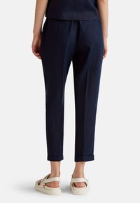 Navy blue linen trousers with an elastic waistband, cuffed hems, and side pockets. Worn with light-colored sandals.