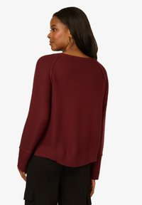 Bordeauxfarbener Strickpullover mit rundem Halsausschnitt, geripptem Saum und langen Ärmeln, der mit strukturierter Stoffqualität und einem entspannten Schnitt überzeugt.