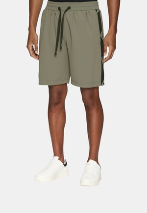 Olivenfarvede atletiske shorts med elastisk talje, snor, sidepaneldetaljer og en glat overflade. Sammen med hvide sneakers.