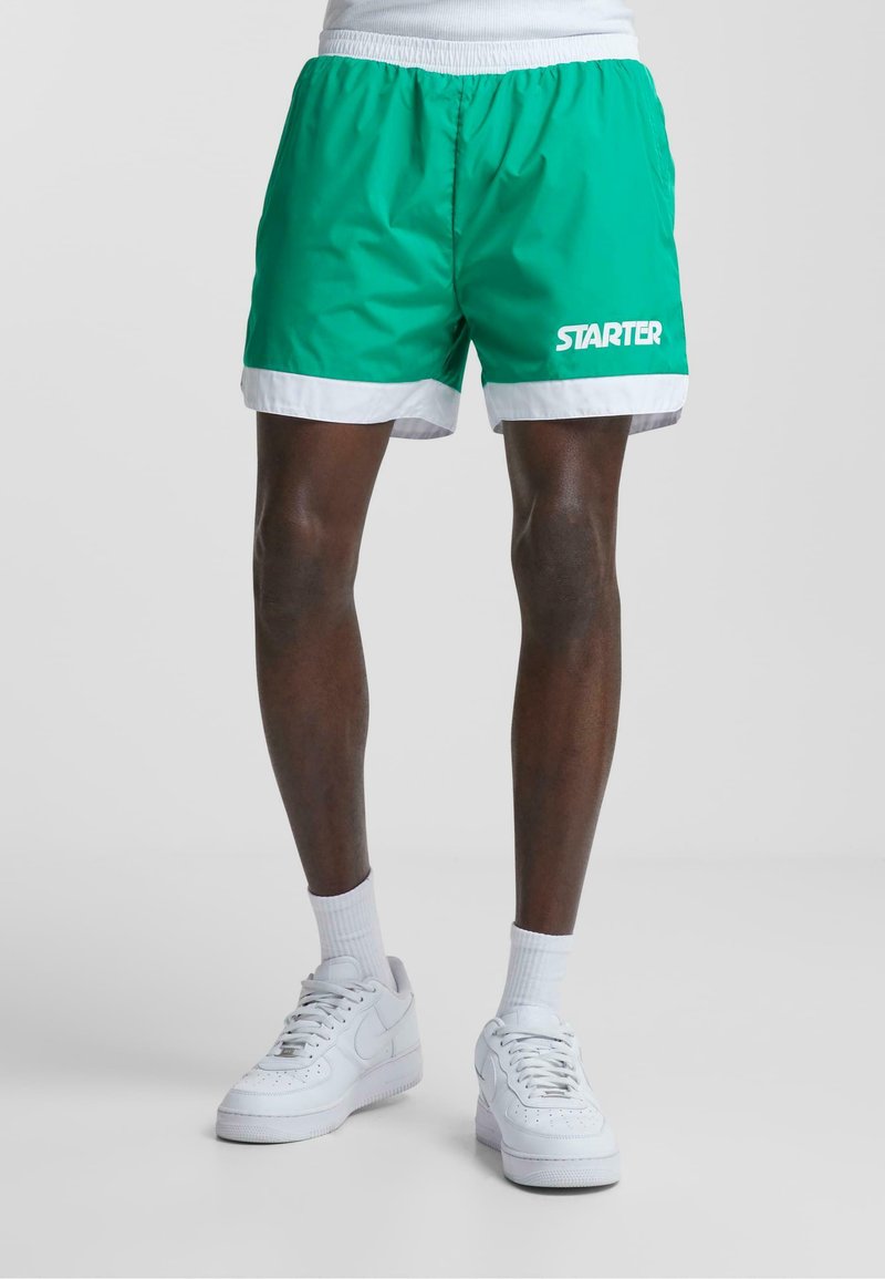 Grønne atletiske shorts med hvide kanter og "STARTER" logoet i hvid. Har et letvægtsmateriale og en elastisk talje.