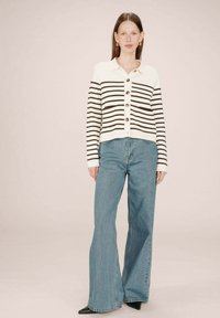 Cardigan rayé en crème et marron avec une fermeture à boutons, assorti à un jean clair évasé et des chaussures noires à talons pointus.