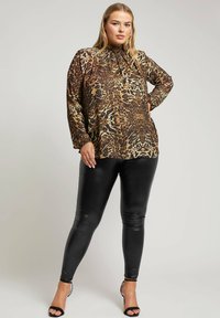 Blusa a manica lunga con stampa leopardata e scollo arricciato; abbinata a leggings neri aderenti e lucidi e tacchi alti neri con cinturini.