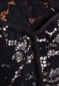 Musta pitsikangas, jossa on kukkakuoseja ja sileät mustat reunat. Monimutkainen malli esittää läpikuultavia osia tumman taustan vasten.