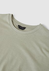 T-shirt di cotone verde chiaro con colletto tondo, texture liscia e un'etichetta nera interna che riporta il nome del marchio "CALLIOPE" e la taglia "L".
