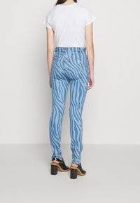 Jeans de mezclilla azul claro con un patrón de rayas de cebra, corte ajustado, diseño de cintura alta y bolsillos traseros. Combinados con zapatos de tacón negros.