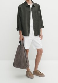 Groen overhemd met knopen, witte korte broek, grijze suède tas en beige schoenen. Heeft een losse pasvorm met opgerolde mouwen en een borstzak.