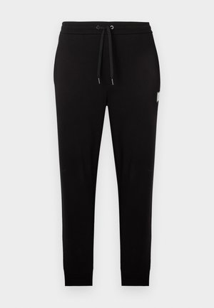 Black slim-fit jogger pants with elastic waistband, black drawstring, and a small rectangular patch on the right thigh.