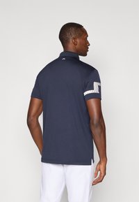 Mørkeblå polo skjorte med krave, korte ermer og hvit detalj på venstre erme. Glatt tekstur og skreddersydd passform.