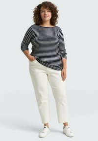 Marineblau- und weiße gestreifte Langarmbluse, kombiniert mit off-white tapered Pants und weißen Sneakers. Sanfter Stoff, lässige Passform und seitliche Taschen.