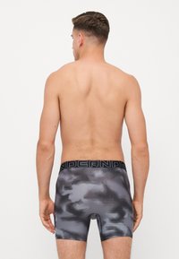 Herren Boxershorts im grauen Camouflage-Muster mit einem schwarzen elastischen Bund, der den Schriftzug "UNDER" trägt. Glatte, dehnbare Stoffqualität.