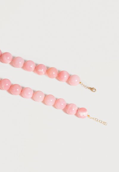 Collier de perles rondes roses brillantes avec fermoir mousqueton doré et chaîne ajustable sur un fond clair, disposé en diagonale.