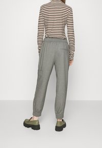 Gray, relaxed-fit trousers with an elastic waistband and elastic cuffs. Accented by a side pocket and paired with olive green footwear.